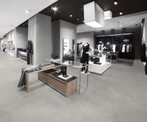 clothing store with grey commercial tile flooring, grey walls and bright lighting on the ceiling.
